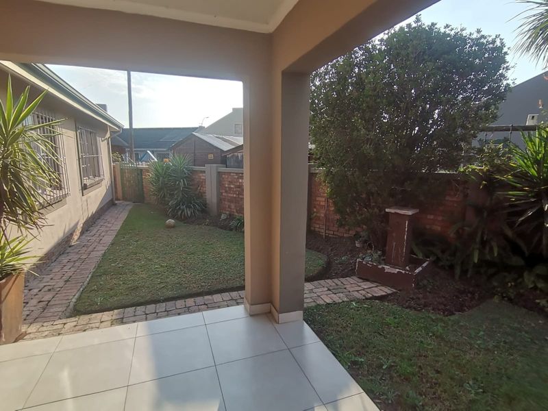 A covered patio area featuring tiled flooring, overlooking a small private garden with a brick boundary wall and paved pathway.