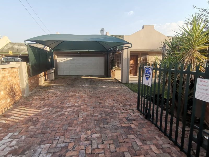 Front view of the property featuring a paved driveway, a shade cloth carport, a sectional garage door, and secure metal gate access.