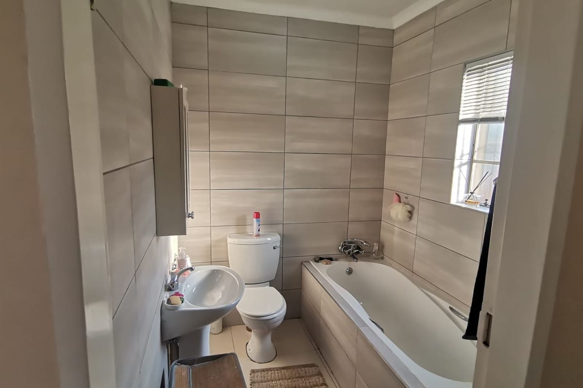 A functional bathroom featuring full-height wall tiling, a pedestal basin, a toilet, and a bathtub with integrated fixtures.