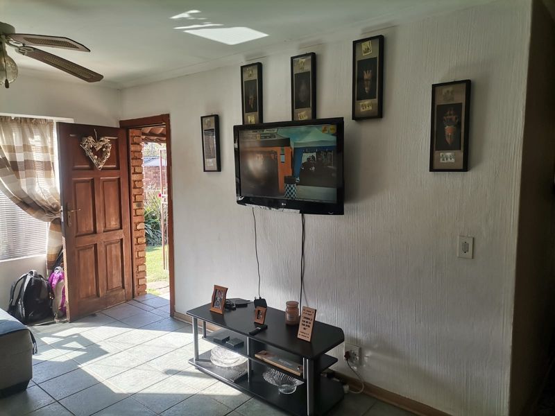 A living room area featuring tiled flooring, a ceiling fan, and direct access to an outdoor space through a timber door.