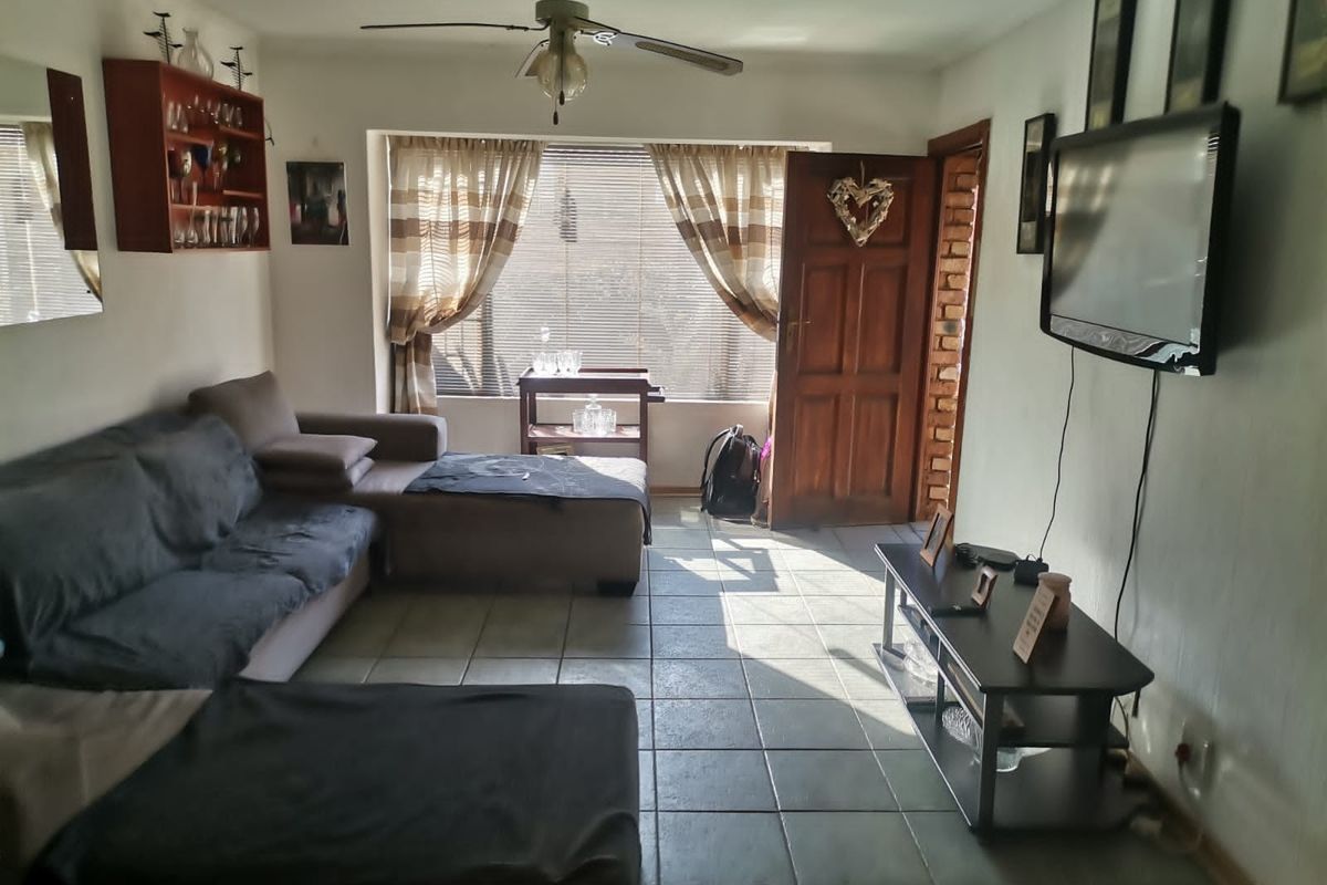A living room featuring tiled flooring, a ceiling fan, and natural light through a window with blinds and a timber entrance door.