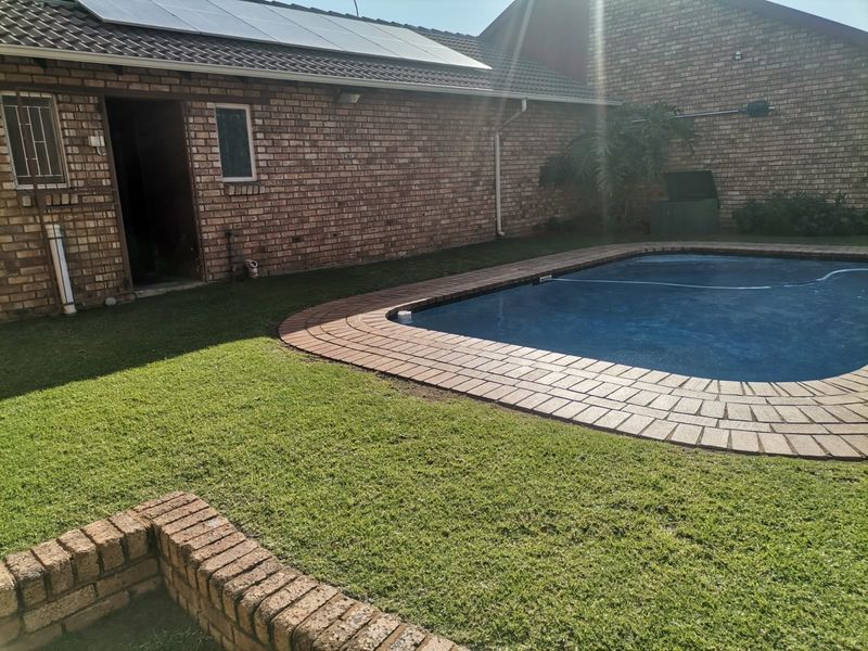 A private backyard area featuring a swimming pool with brick paving, surrounded by a well-maintained lawn and brick townhouse exterior walls.