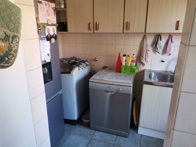 A functional laundry area featuring built-in cabinetry, a stainless steel sink, tiled splashback, and tiled flooring with space for laundry appliances.