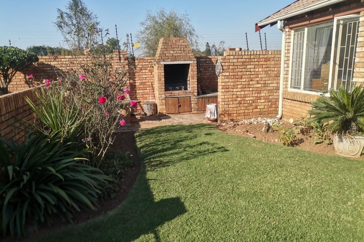 A private rear garden featuring a built-in brick braai, paved entertainment area, well-maintained lawn, and secure brick boundary walls with electric fencing.