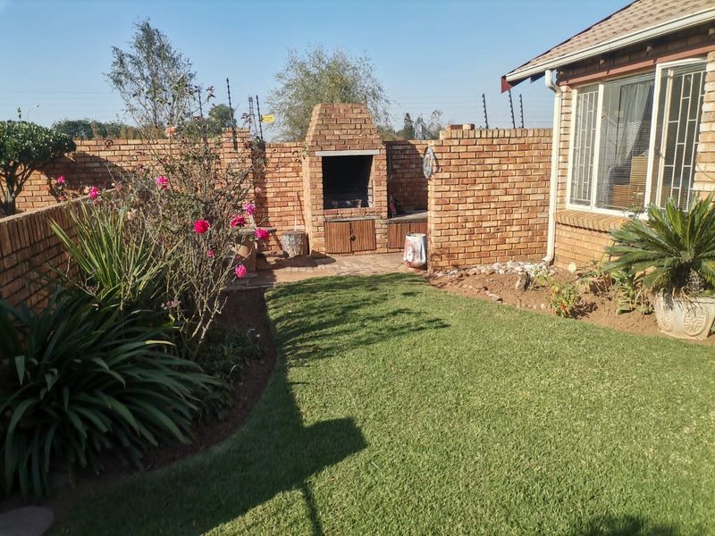 A private rear garden featuring a built-in brick braai, paved entertainment area, well-maintained lawn, and secure brick boundary walls with electric fencing.