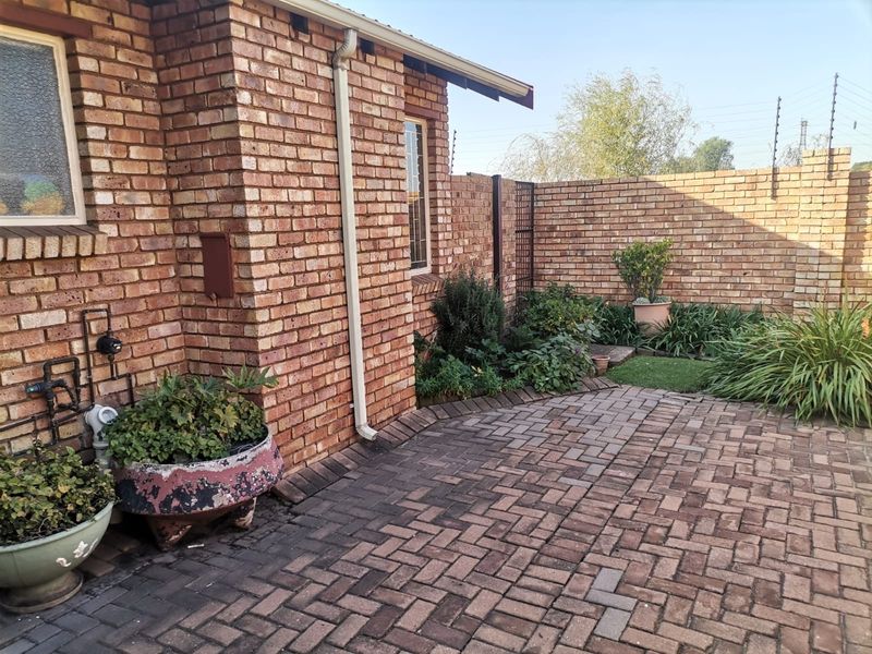 A private rear courtyard featuring face brick walls, paved flooring, and established garden beds with perimeter security fencing.