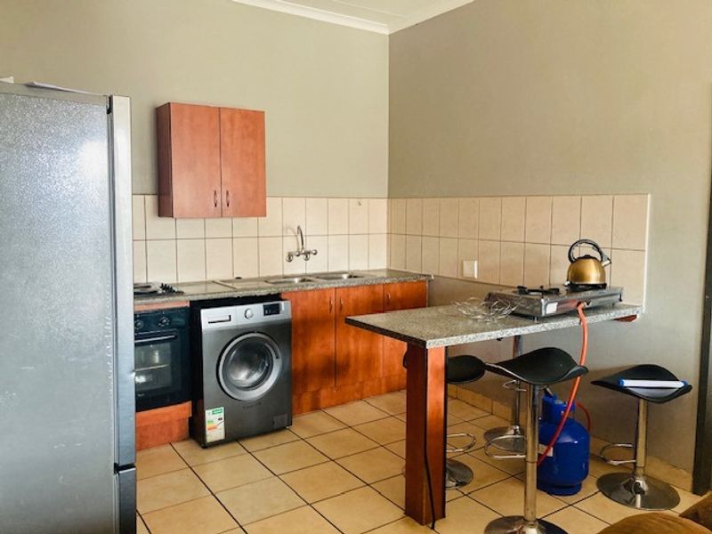 A functional kitchen featuring wood-finish cabinetry, tiled backsplash, built-in oven, and a breakfast bar with tiled flooring throughout.