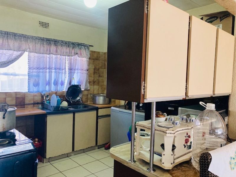 A functional kitchen featuring dated cabinetry, tiled backsplash, and ceramic flooring, offering potential for modernization and aesthetic updates.