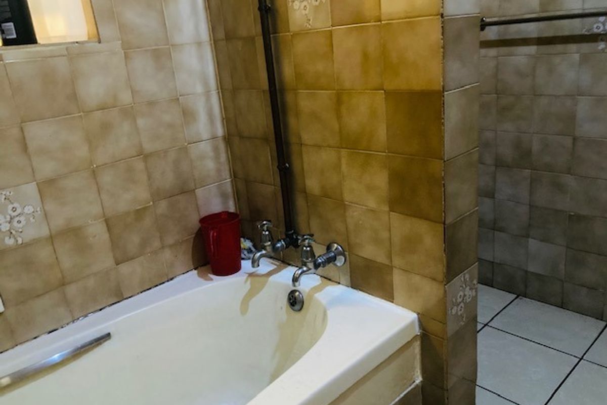A dated bathroom featuring a bathtub with exposed plumbing, ceramic wall and floor tiles, and a towel rail.