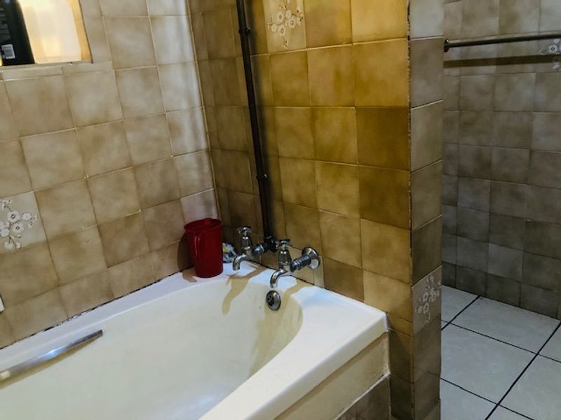 A dated bathroom featuring a bathtub with exposed plumbing, ceramic wall and floor tiles, and a towel rail.