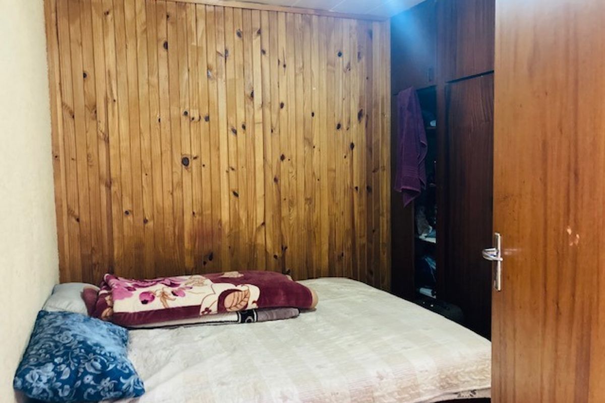 A bedroom featuring timber wall paneling and built-in wooden cupboards, offering a dated aesthetic that could benefit from modern updates.