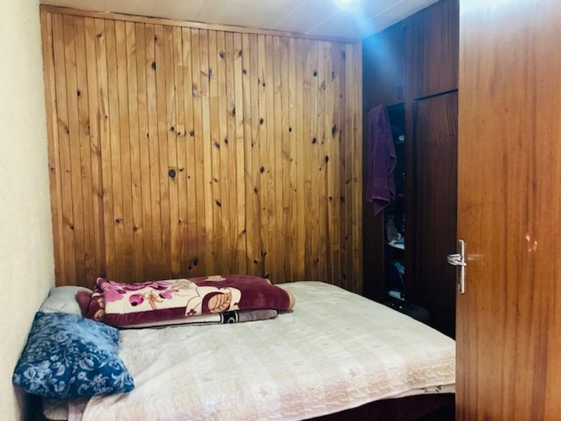 A bedroom featuring timber wall paneling and built-in wooden cupboards, offering a dated aesthetic that could benefit from modern updates.
