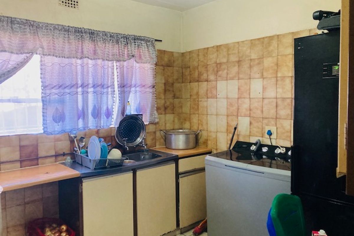 A functional kitchen area featuring built-in cabinetry, a stainless steel sink, and tiled wall finishes, offering potential for modernization and aesthetic improvement.