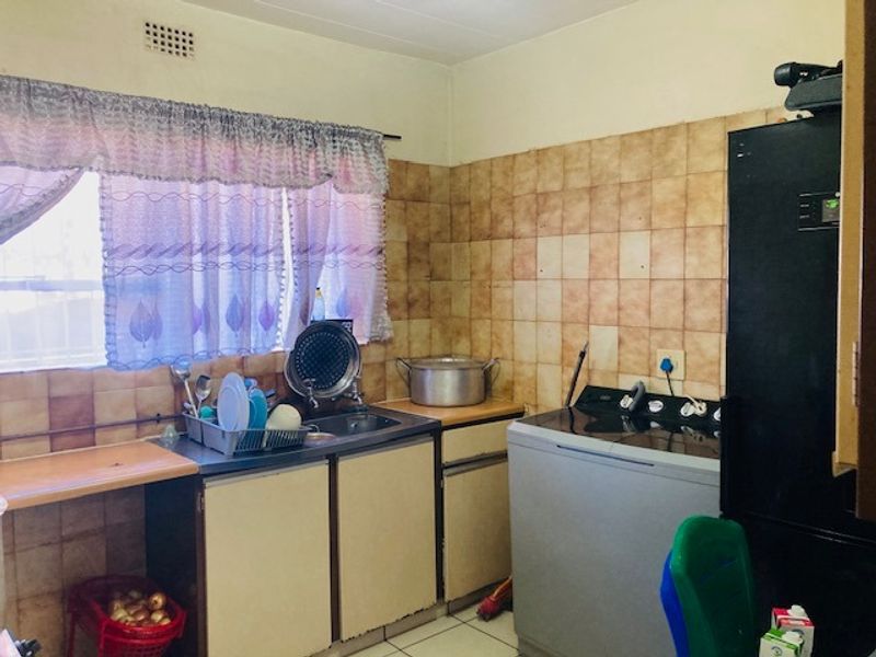 A functional kitchen area featuring built-in cabinetry, a stainless steel sink, and tiled wall finishes, offering potential for modernization and aesthetic improvement.