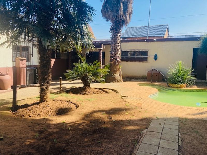 Rear garden area featuring a swimming pool with paved surround, mature palm trees, and perimeter boundary walls with security features.