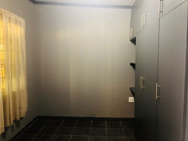 A compact bedroom featuring dark tiled flooring, grey walls, and built-in storage cupboards.