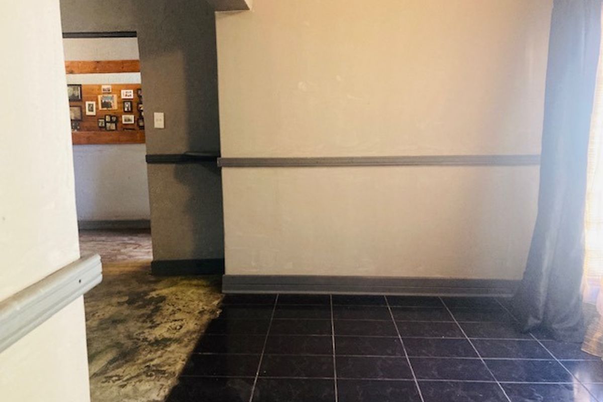 An empty living area featuring dark ceramic floor tiles, chair rail molding, and neutral wall paint, showing signs of wear and requiring cosmetic updates.