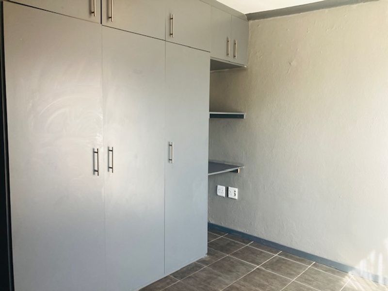 A bedroom featuring built-in grey cupboards, tiled flooring, and a small integrated desk area with electrical points.