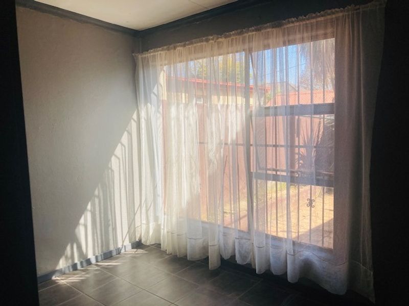 An empty bedroom featuring tiled flooring and a large sliding glass door with security gate, providing access to the exterior.