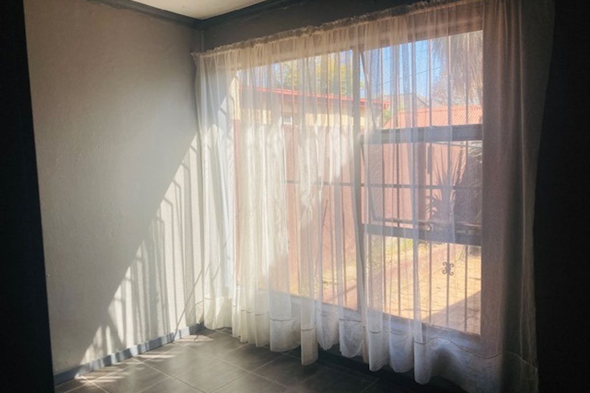 An empty bedroom featuring tiled flooring and a large sliding glass door with security gate, providing access to the exterior.