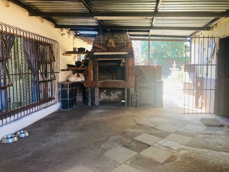 Covered outdoor patio area featuring a built-in brick braai, metal roofing, and security bars, offering a functional space for outdoor entertaining.