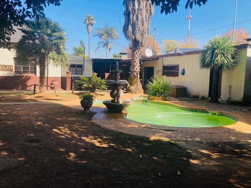 Outdoor pool area featuring a central water fountain, brick paving, and established garden elements, requiring maintenance to the pool and surrounding exterior surfaces.