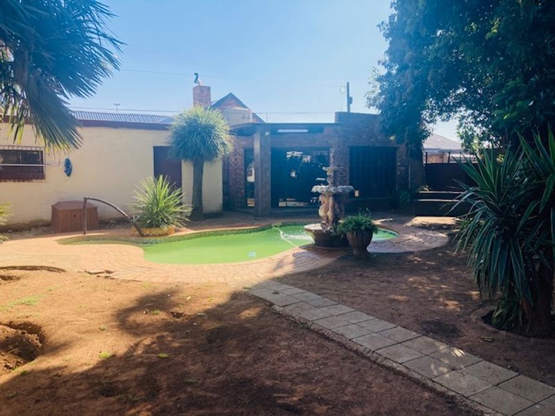 Rear garden area featuring a swimming pool with a central water fountain, brick paving, and established landscaping against the rear building facade.
