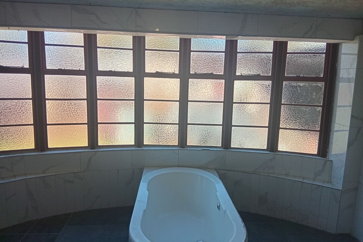 A bathroom featuring a built-in bathtub positioned beneath a large multi-pane window with textured glass and tiled wall surrounds.