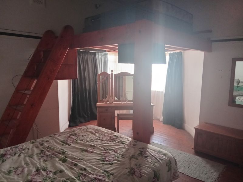 A bedroom featuring timber flooring and a built-in loft structure with an integrated ladder, offering a unique layout for sleeping or storage.