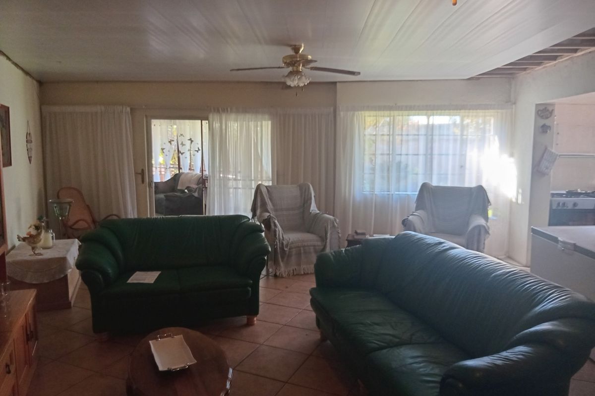 Spacious living room featuring tiled flooring, a ceiling fan, and sliding glass doors leading to the exterior, with some visible ceiling maintenance required.