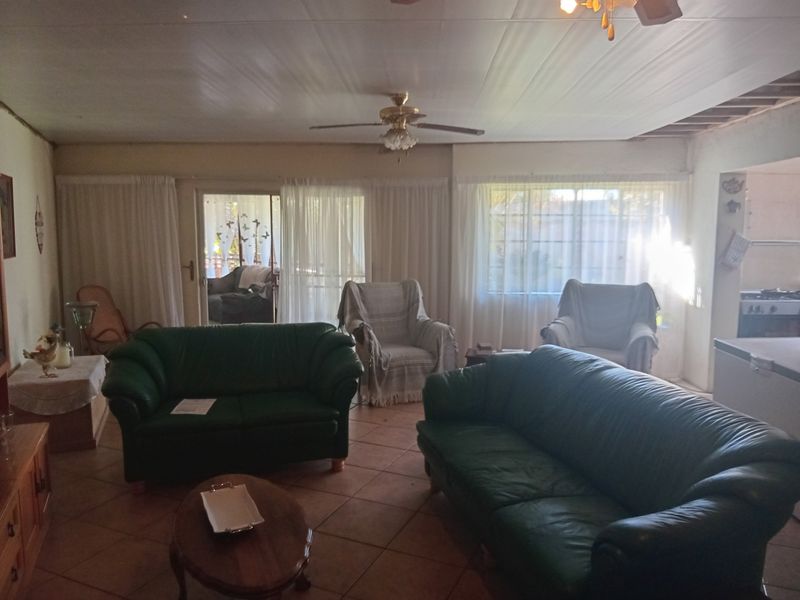 Spacious living room featuring tiled flooring, a ceiling fan, and sliding glass doors leading to the exterior, with some visible ceiling maintenance required.