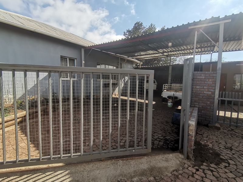 Front exterior view featuring a metal security gate, paved driveway, and a covered carport area.