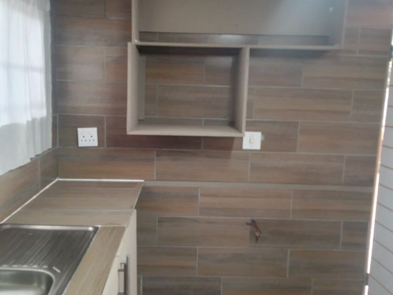 A compact kitchen area featuring wood-look tiled walls, built-in cabinetry, and a stainless steel sink, currently awaiting final appliance installation.
