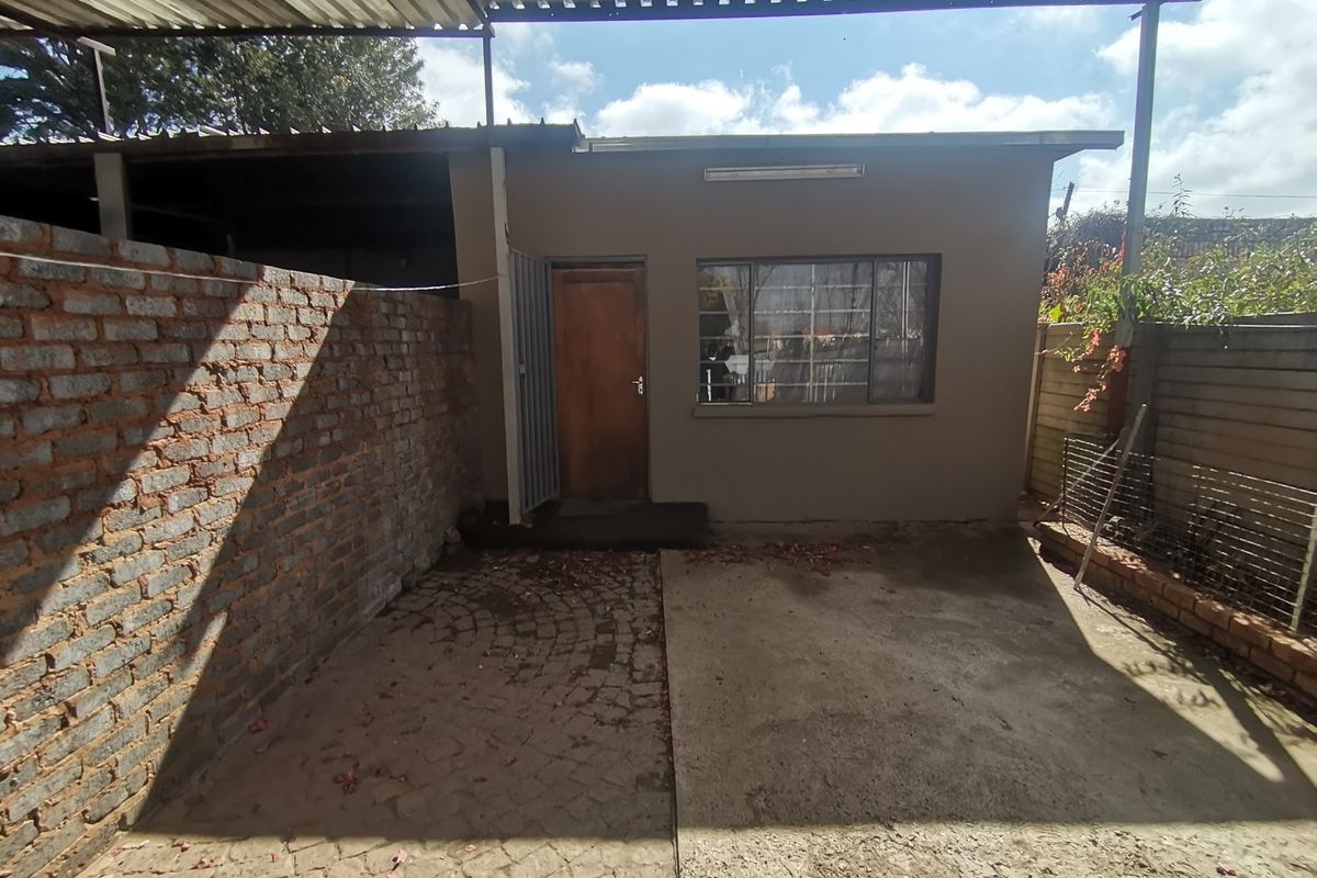 Rear exterior view of the property featuring a covered patio area, brick boundary wall, and concrete paving.