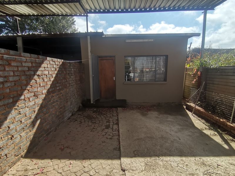 Rear exterior view of the property featuring a covered patio area, brick boundary wall, and concrete paving.