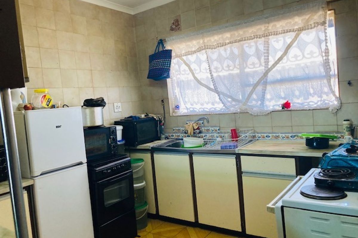 A functional kitchen featuring dated cabinetry, tiled backsplash, and a stainless steel sink, offering potential for modernization and renovation.