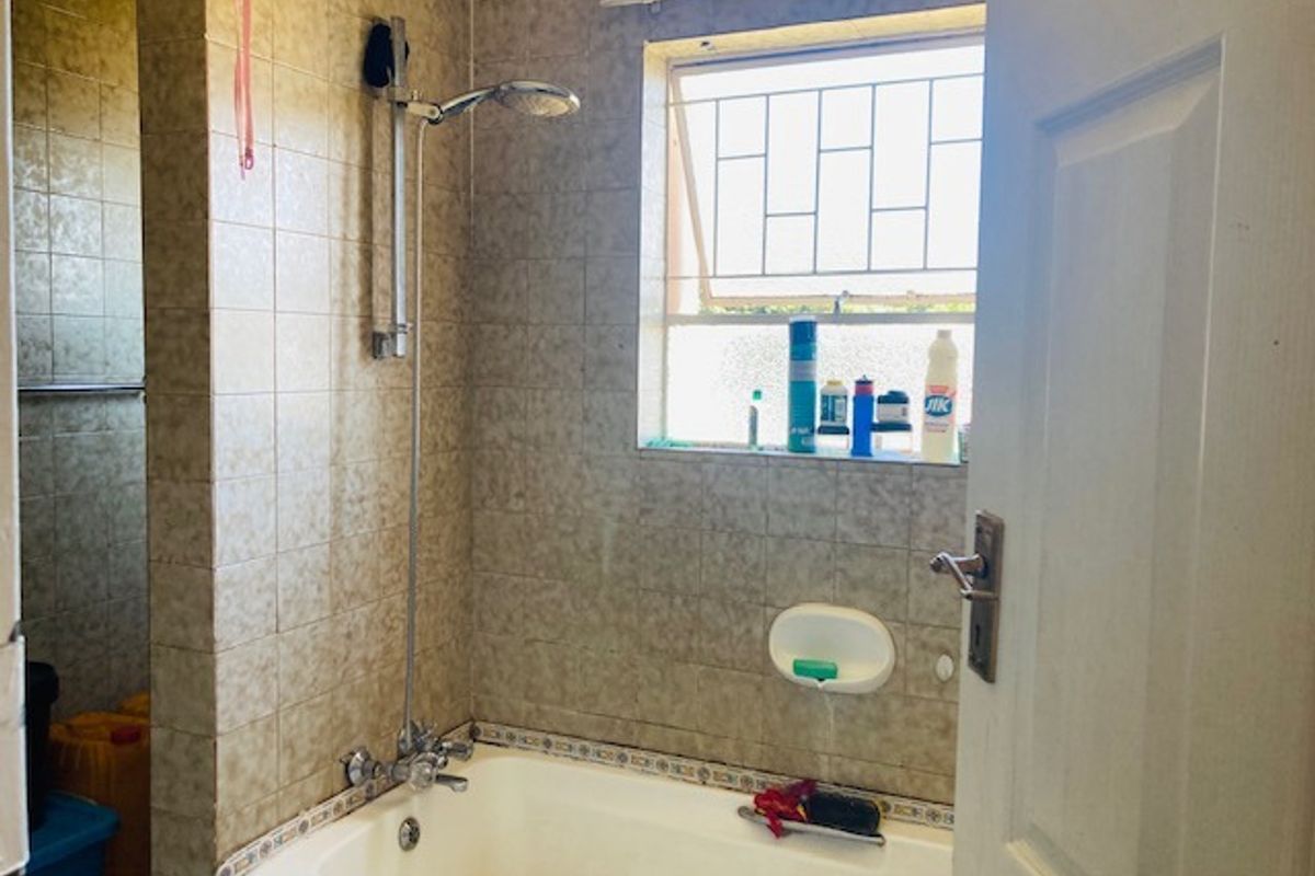 A functional bathroom featuring a bathtub with a shower attachment, tiled walls, and a window with security bars.