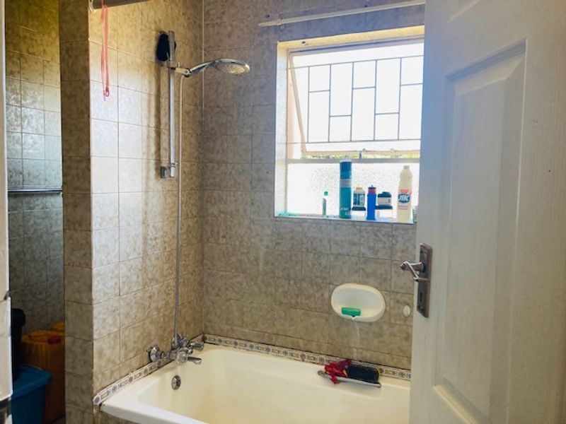 A functional bathroom featuring a bathtub with a shower attachment, tiled walls, and a window with security bars.