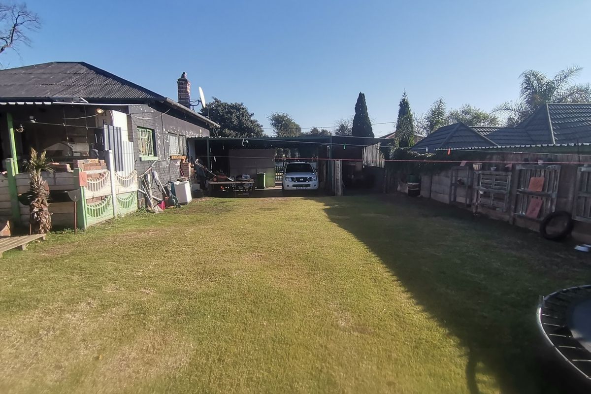 A rear garden view featuring a lawn, perimeter fencing, and a covered carport area attached to the main dwelling.