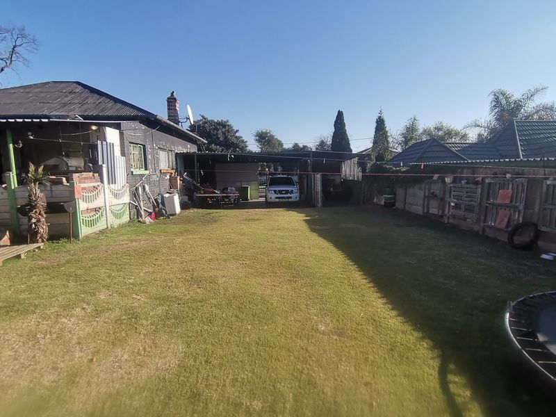 A rear garden view featuring a lawn, perimeter fencing, and a covered carport area attached to the main dwelling.