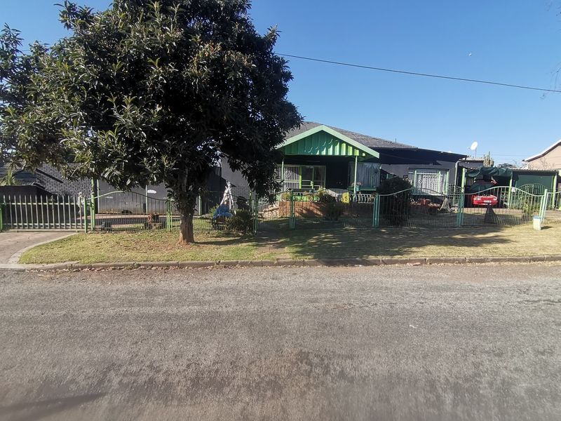 Front view of a single-story house featuring a gabled porch, metal perimeter fencing, and a driveway, set on a residential street.