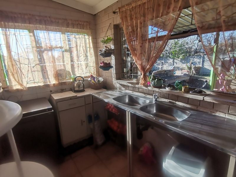 A functional scullery area featuring a double stainless steel sink, exposed brick walls, and direct access to the rear garden area.