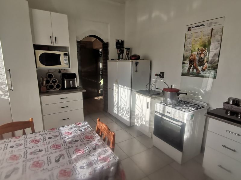 A functional kitchen featuring white cabinetry, a gas stove with oven, and tiled flooring, leading through an arched doorway to adjacent living spaces.