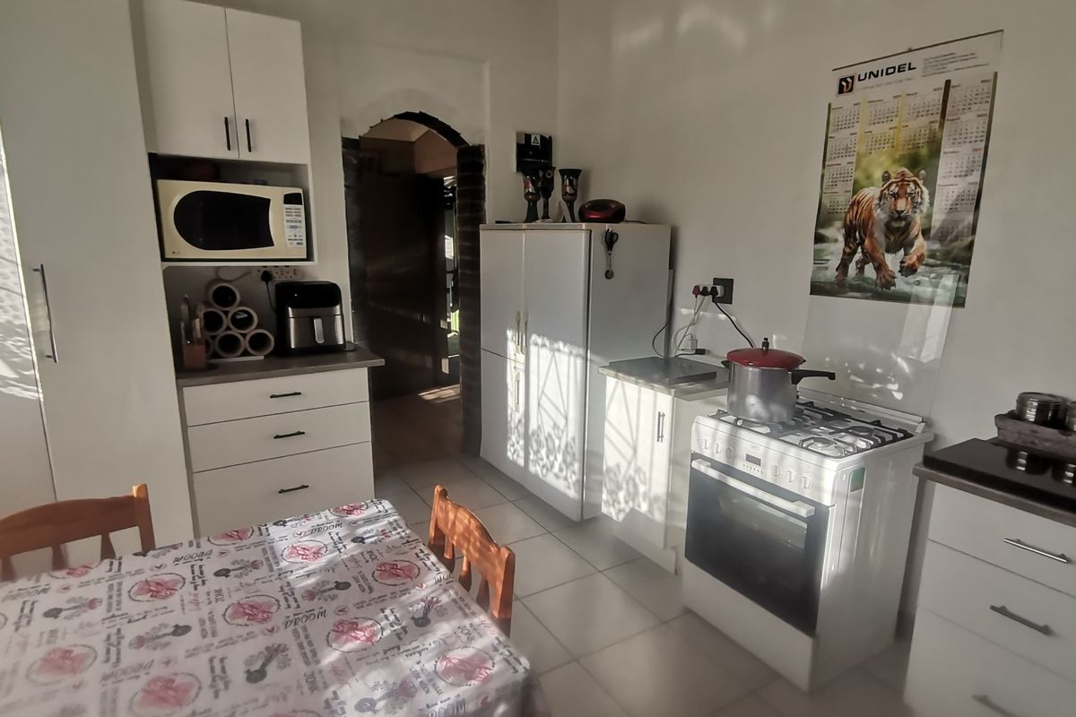 A functional kitchen featuring white cabinetry, a gas stove with oven, and tiled flooring, leading through an arched doorway to adjacent living spaces.