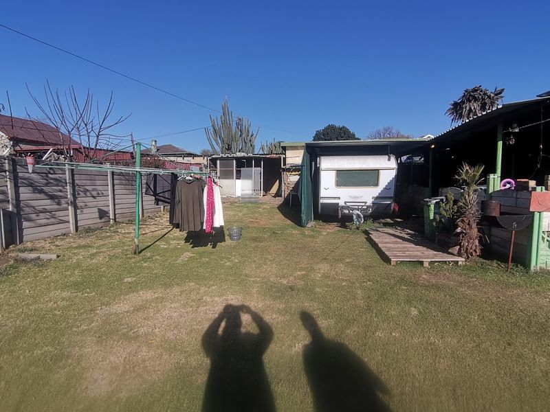 A rear garden area featuring a lawn, a precast concrete boundary wall, and a covered carport structure.