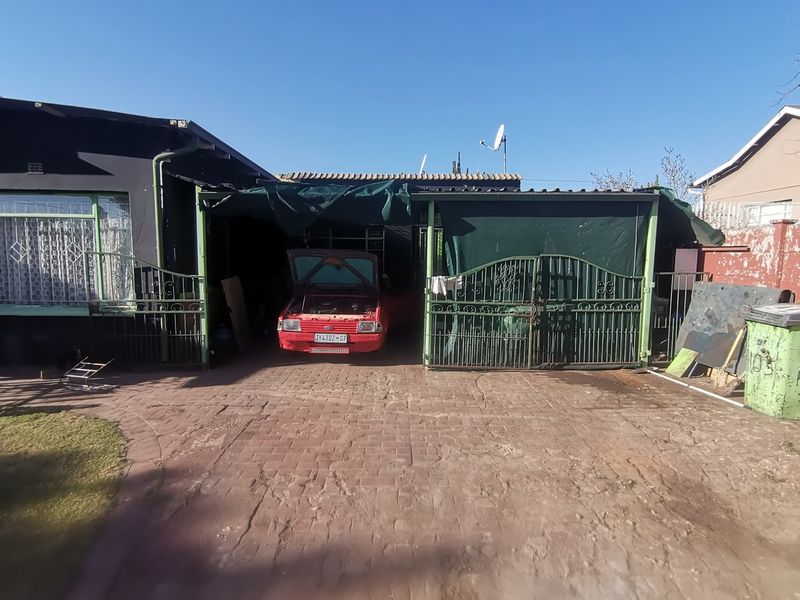 A residential property featuring a paved driveway leading to a covered carport area with metal security gates.