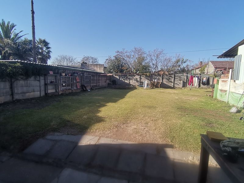 A spacious rear garden featuring a large lawn area, paved patio section, and precast concrete boundary walls.