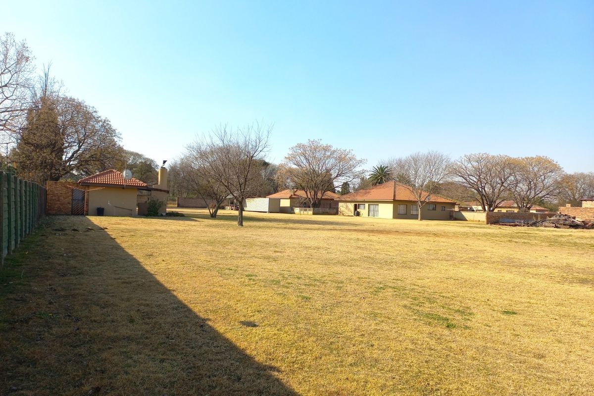 A wide view of the rear property grounds featuring expansive lawn space, mature trees, and multiple outbuildings with tiled roofs.