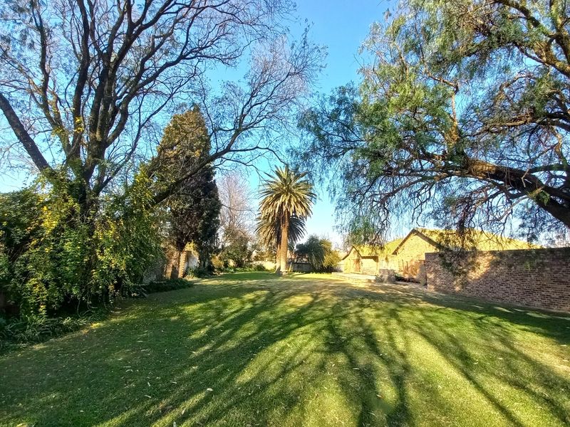 A spacious, well-maintained garden area featuring mature trees, a lush lawn, and a traditional brick boundary wall on a farm property.