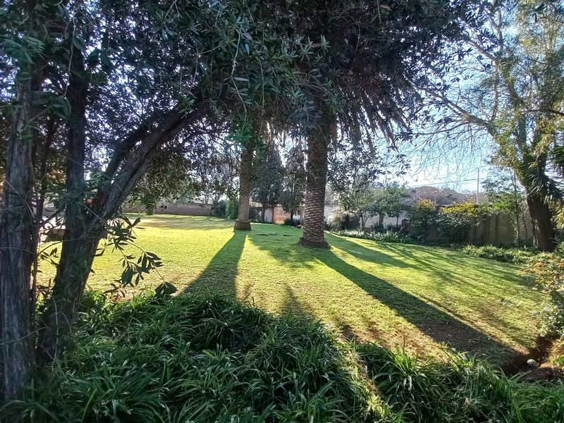 A spacious, well-maintained garden featuring mature trees, expansive lawn areas, and secure perimeter walling, offering a peaceful outdoor setting.